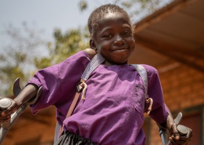 Niña de República Centroafricana andando con muletas muy sonriente